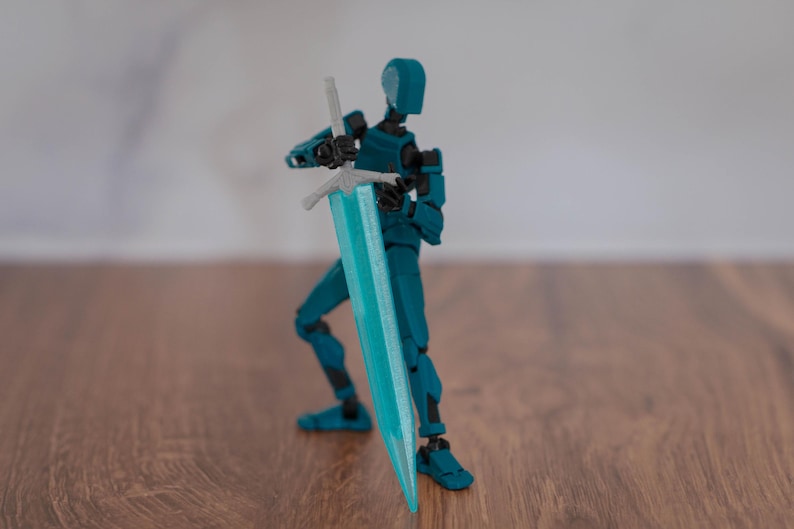 Puede incluir: Una figura de acci&oacute;n articulada de color azul turquesa sosteniendo una espada azul turquesa con una empu&ntilde;adura plateada. La figura est&aacute; de pie sobre una superficie de madera.