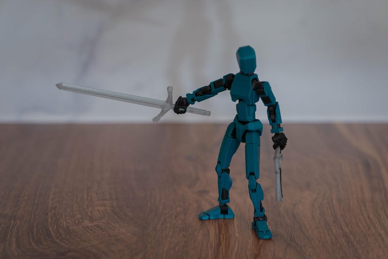 Puede incluir: Una figura de acci&oacute;n articulada de color azul turquesa que sostiene una espada plateada y una pistola plateada. La figura est&aacute; de pie sobre una superficie de madera.