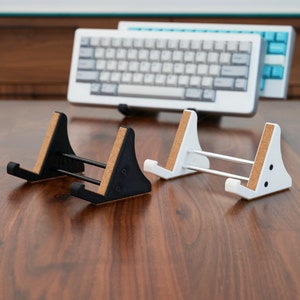 May include: Two keyboard stands, one black and one white, with cork pads on the bottom. The stands are made of plastic and have a simple design.