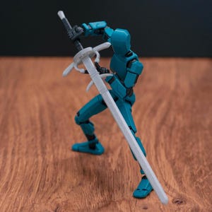 Könnte beinhalten: Eine tealblaue, artikulierte Actionfigur, die ein weißes Plastik-Schwert hält. Die Figur ist in Kampfstellung mit dem Schwert über dem Kopf.