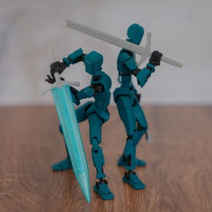 Op de afbeelding: Twee tealblauwe, gearticuleerde actieve figuren die zwaarden vasthouden. Eén figuur houdt een zilveren zwaard vast, de andere een tealblauw zwaard.
