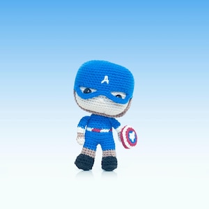 Puede incluir: Un juguete de amigurumi de crochet azul de Capitán América, con un traje rojo, blanco y azul y sosteniendo un escudo rojo, blanco y azul.