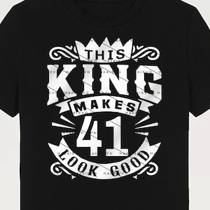 May include: Black and white graphic design on a black t-shirt. The design features a crown, the words "This King Makes 41 Look Good", and decorative flourishes.