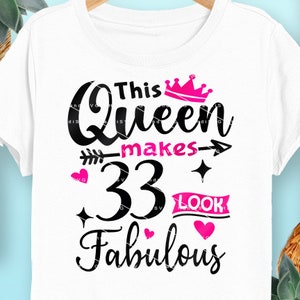 Op de afbeelding: Een wit T-shirt met zwarte tekst die "This Queen makes 33 look fabulous" luidt. De tekst is versierd met een roze kroon, een roze pijl en roze harten.
