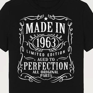 以下が含まれることがあります： 「Made in 1963 Limited Edition Aged to Perfection All Original Parts」と白で書かれたヴィンテージ風のグラフィックがプリントされた黒いTシャツ。