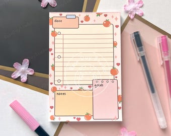 May include: A notepad with a peach and heart pattern. The notepad has sections labeled "date", "notes", and "goals". The notepad is decorated with illustrations of peaches and hearts. Two pens and a pink marker are in the background.
