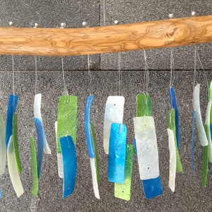 May include: A wooden wind chime with multiple hanging glass pieces in shades of blue and green. The glass pieces are rectangular and have a translucent, iridescent finish.