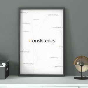 Peut inclure: Une affiche encadrée avec le mot "Consistency" en or et noir, sur fond blanc avec un motif géométrique. L'affiche est dans un cadre noir, exposée sur une surface blanche.