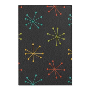 May include: A rectangular rug with a dark gray background and a repeating pattern of colorful starbursts. The starbursts are in shades of teal, yellow, orange, and green. The rug has a textured appearance.