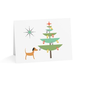 May include: A brown and white dog looks up at a green Christmas tree with red, yellow, and white ornaments. A silver star is in the background.