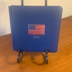 May include: A navy blue hardcover book with a silver American flag and the word "glory" printed on the front cover.