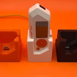 May include: Three charging stands for a white device with the word "FLIPPI" printed on it. The stands are orange, white, and black.