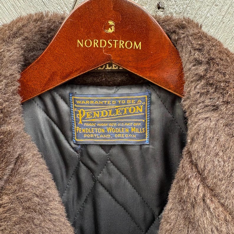 May include: Close-up of a brown Pendleton wool coat with a dark quilted lining. The coat is on a wooden Nordstrom hanger. A blue and gold Pendleton label is visible, along with the Nordstrom logo.