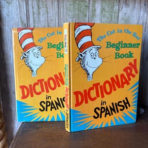 May include: Two copies of "The Cat in the Hat Beginner Book Dictionary in Spanish" are displayed. The books have bright yellow covers with the Cat in the Hat character and text in English and Spanish. The spines are visible.