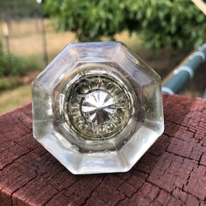 May include: Clear, octagonal glass doorknob with a decorative center. The knob has a faceted design, reflecting light. The doorknob is likely vintage or antique, adding a touch of classic style to any door.