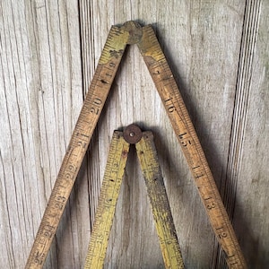 May include: Two antique wooden folding rulers, one larger and one smaller, are displayed against a weathered wooden background. The rulers are marked with inch measurements, showing signs of age and wear. The larger ruler extends to 24 inches.