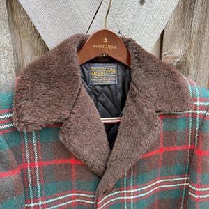 May include: A Pendleton plaid jacket with a brown faux fur collar. The jacket features a green, red, and brown plaid pattern. The collar is a dark brown color. The jacket is hanging on a wooden hanger with the Nordstrom logo.