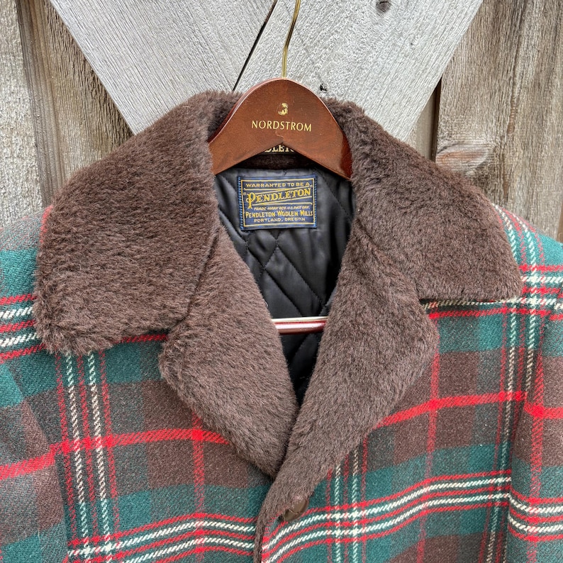 May include: A Pendleton plaid jacket with a brown faux fur collar. The jacket features a green, red, and brown plaid pattern. The collar is a dark brown color. The jacket is hanging on a wooden hanger with the Nordstrom logo.