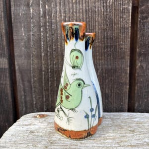 May include: A pair of ceramic vases with a hand-painted design. The vases are white with a brown base and rim. One vase features a green bird and butterfly, with the word "Mexico" at the base. The other vase has a blue stripe.