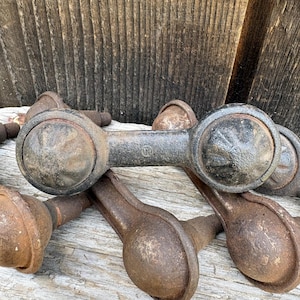 May include: Close-up of several antique, cast iron door handles. The handles have a dark, weathered appearance with a circular design on each end and a connecting bar. The metal has a rustic, aged look, suggesting they are vintage.
