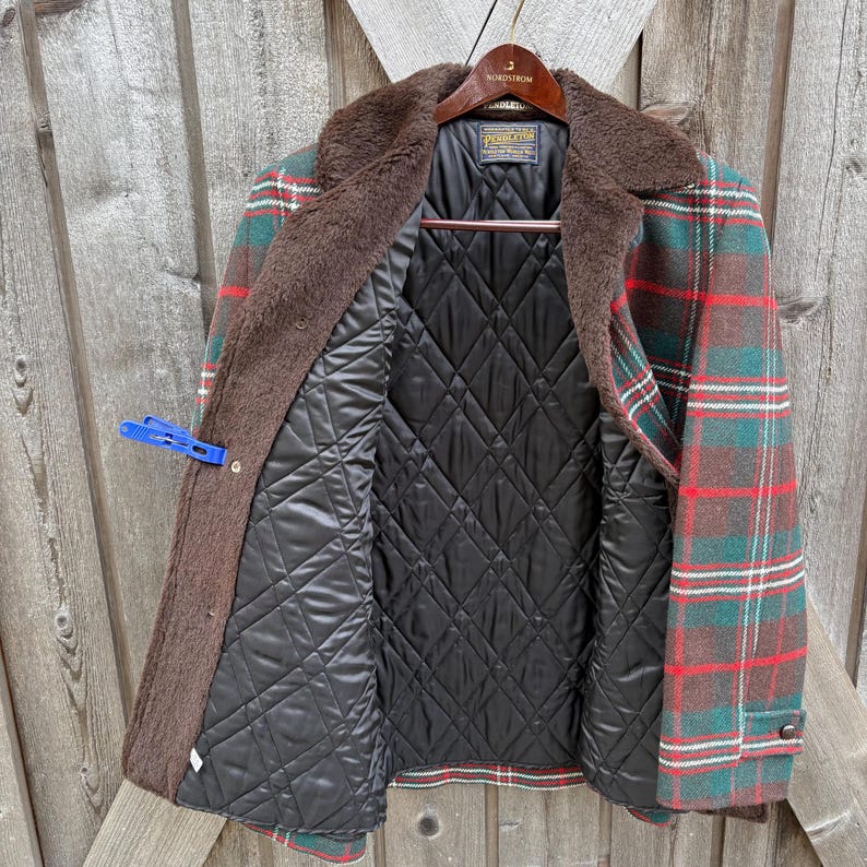 May include: A Pendleton plaid jacket with a brown faux fur collar and a black quilted lining. The jacket features a red, green, and white plaid pattern. The jacket is open, revealing the interior lining and the Pendleton label.