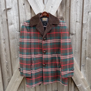 May include: A vintage plaid coat in shades of green, red, and brown, with a faux fur collar. The coat features a button-up front, two front pockets, and buttoned cuffs. The coat is hanging on a wooden hanger.
