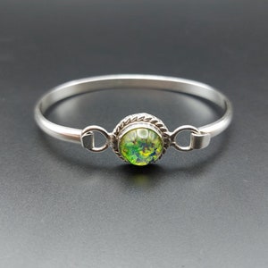 May include: A silver bangle bracelet with a green opal gemstone set in a silver bezel.