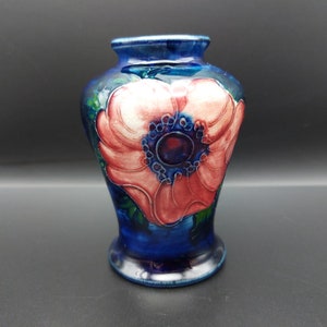 May include: A blue and white ceramic vase with a pink flower design. The vase has a rounded body and a flared lip.