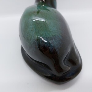 May include: A ceramic figurine of a sleeping cat with a black and green glaze. The cat is lying on its side with its head resting on its paws.