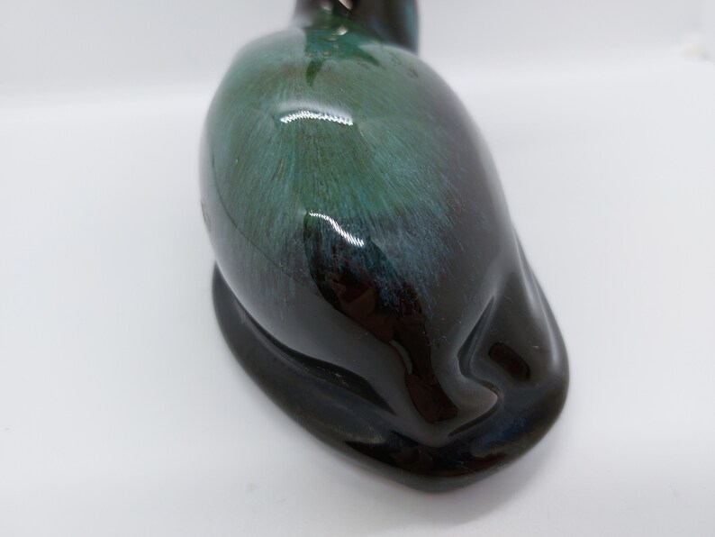 May include: A ceramic figurine of a sleeping cat with a black and green glaze. The cat is lying on its side with its head resting on its paws.