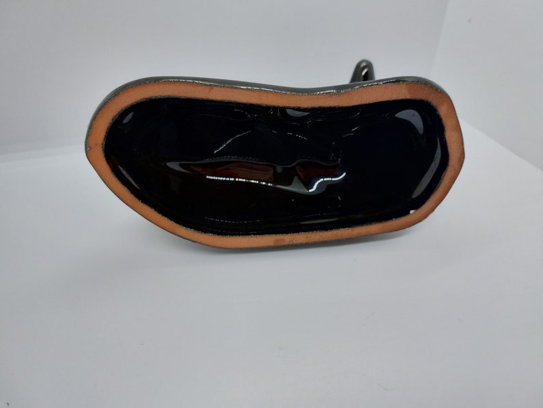 May include: The bottom of a black ceramic figurine with a brown rim. The figurine is glazed and has a smooth, shiny finish.