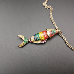 May include: A gold chain necklace with a colourful enamel fish pendant. The fish is red, yellow, green, and blue.