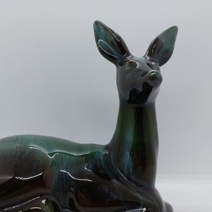 May include: A ceramic deer figurine in a dark green and blue glaze. The deer is lying down with its head turned to the side.