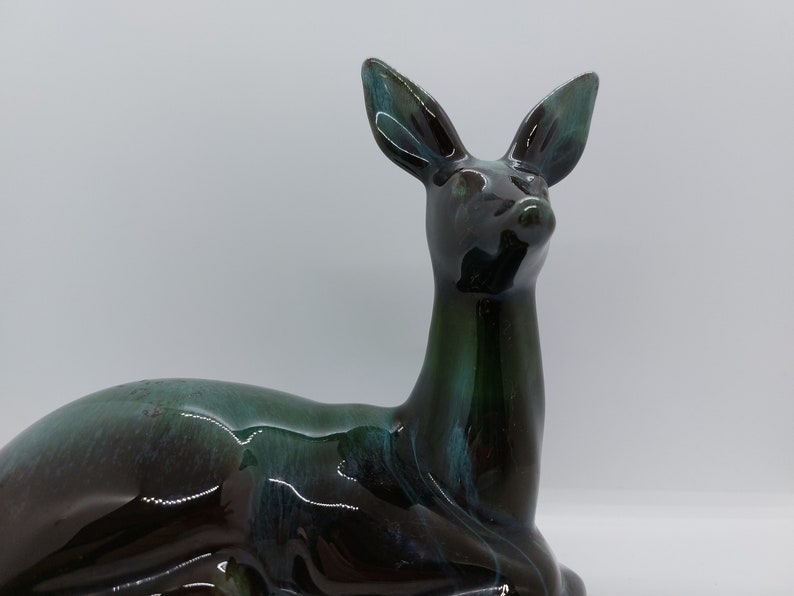 May include: A ceramic deer figurine in a dark green and blue glaze. The deer is lying down with its head turned to the side.
