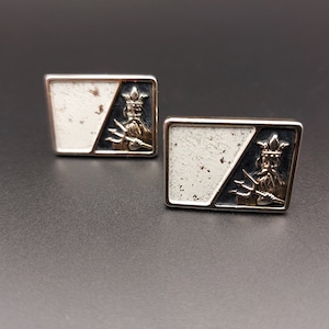 Peut inclure: Une paire de boutons de manchette en argent avec un motif blanc et noir. Chaque bouton de manchette présente une image stylisée d'un homme avec une couronne et un trident.