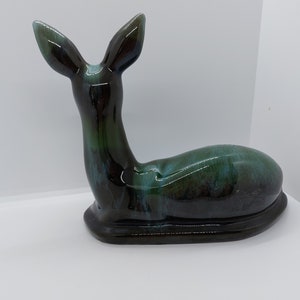May include: A ceramic deer figurine in a black and green glaze. The deer is lying down with its head turned to the side.