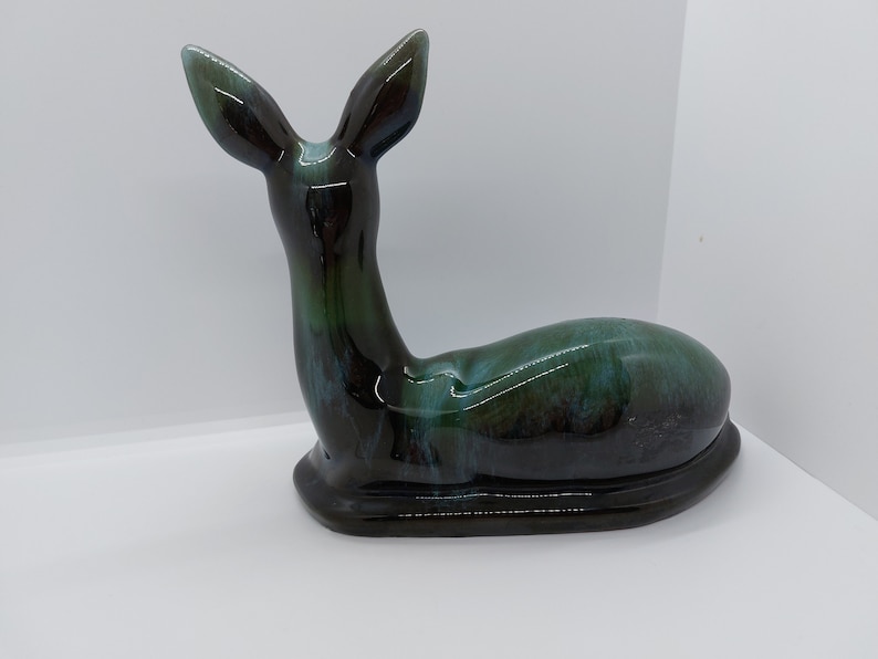 May include: A ceramic deer figurine in a black and green glaze. The deer is lying down with its head turned to the side.