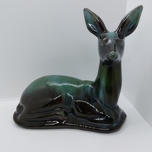 May include: A ceramic deer figurine in a black and green glaze. The deer is lying down with its head raised and its ears perked up.