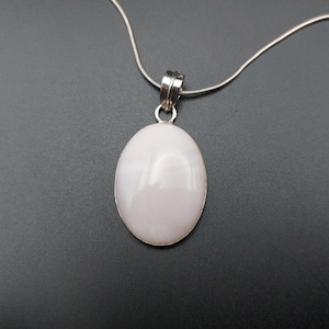 May include: A silver chain necklace with a white oval pendant. The pendant is made of a smooth, opaque material.