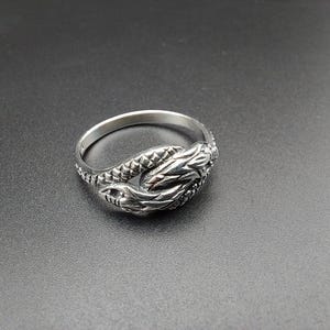 Peut inclure: Une bague en argent avec un motif détaillé d'un serpent s'enroulant autour de lui-même. Les écailles du serpent sont visibles et la bague est polie.