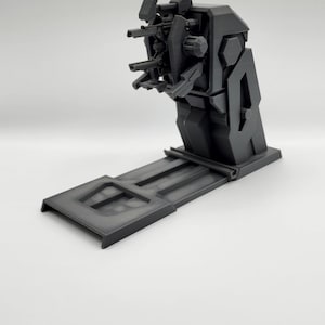 Puede incluir: Un modelo de pl&aacute;stico negro de una torreta de armas futurista con un ca&ntilde;&oacute;n giratorio y varios ca&ntilde;ones. La torreta est&aacute; montada sobre una base de pl&aacute;stico negro.