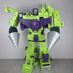 May include: A lime green and purple robot toy with silver drill-shaped arms. The robot has a purple chest piece with a symbol and a black head with red eyes. The toy is a construction vehicle transformer.
