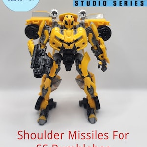 May include: A yellow and black Bumblebee action figure from the Transformers Studio Series. The figure has a detailed design with visible mechanical parts and is posed upright. The text "Shoulder Missiles For SS Bumblebee" is at the bottom.