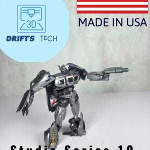 May include: A silver and black robot toy in a robot pose, holding a gun. The toy is labeled "Studio Series 10 Concept Art Pistol".