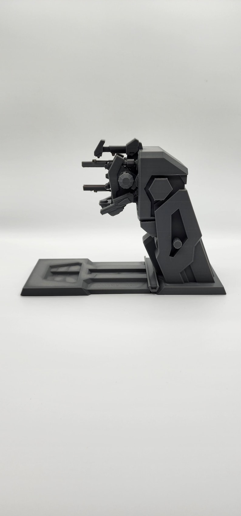 Puede incluir: Un modelo de pl&aacute;stico negro de un arma futurista con una torreta giratoria y varios ca&ntilde;ones. El arma est&aacute; montada sobre una base negra.