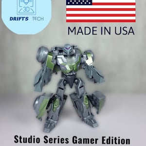 May include: A green and gray robot toy in robot mode. The toy is part of the Studio Series Gamer Edition Soldier Vehicon Conversion Kit. The toy is made in the USA.