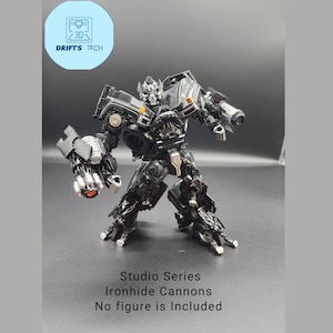 Peut inclure: Cannons Ironhide de la série Studio en noir et argent. Aucune figurine n'est incluse.