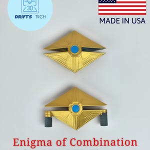 Puede incluir: Dos figuras geométricas doradas con detalles circulares azules. Las figuras tienen forma de diamante con un círculo azul central y están etiquetadas como "Enigma of Combination for SS/AOTP Figures". La imagen también incluye el texto "Made in USA".