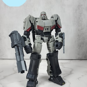 Op de afbeelding: Een grijs en zwart robot speelgoed met een rode borstplaat en een groot pistool. Het speelgoed is gelabeld "TF: One Megatron Upgrade Kit".