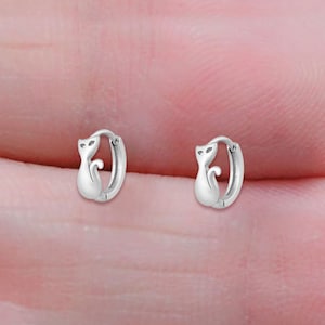 May include: A pair of silver cat-shaped hoop earrings. The earrings are small and delicate, and the cat design is simple and elegant.